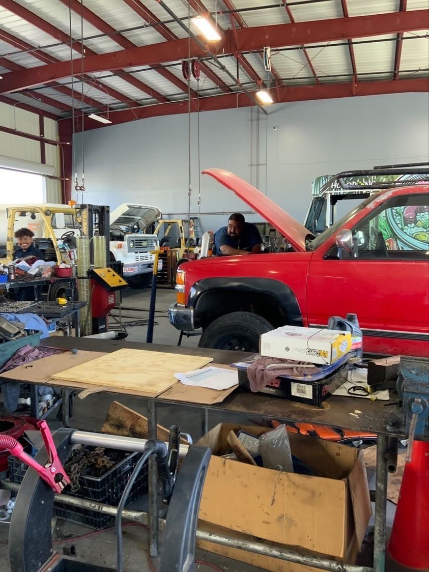 Watsonville Diesel Shop - Two employees are seen, busy working under the hood of a truck, and smiling for the camera. There are a lot of projects going on back here, which is evident from all the open hoods.