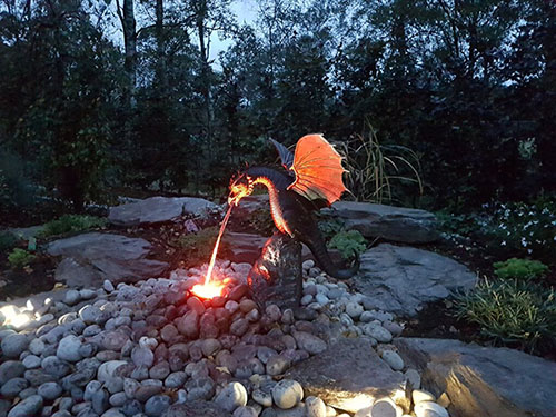 A beautiful dragon, spitting fire, over a bed of rocks, in a garden.