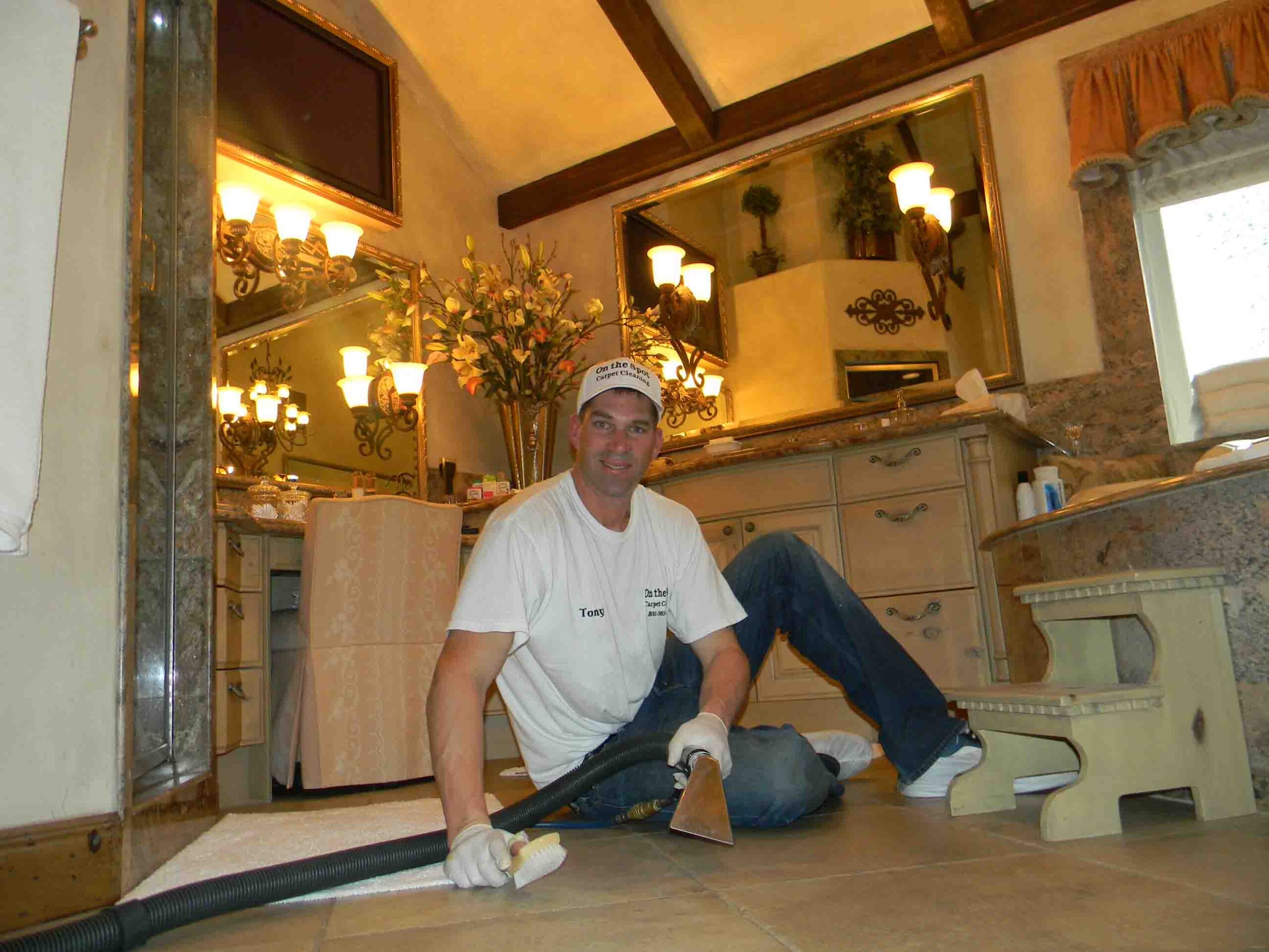 On-The-Spot Cleaning Services - Tony, owner, is sitting in a luxurious bathroom, cleaning the floor. There is a flat-screen mounted on the wall.