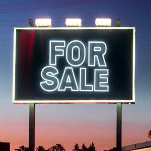 A billboard sign, lit up with the words, "FOR SALE," in the middle.